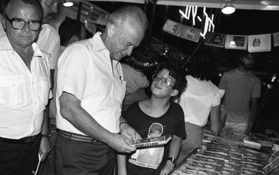 Rabin Itzhak holding a book which he wrote at the Book Fair in Tel Aviv, while his grand son is standing aside