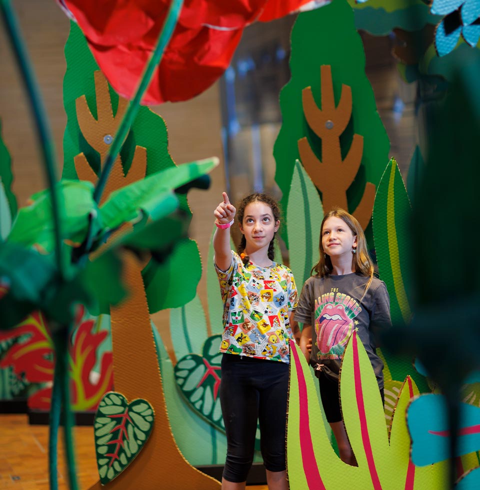 ילדות עומדות בגן הסודי עם פרחי ענק מקרטון